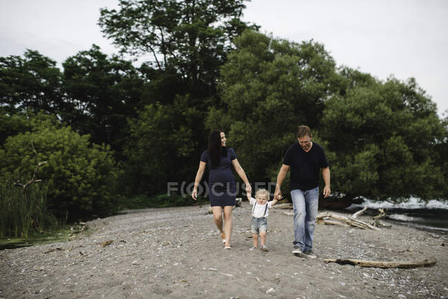 Pareja embarazada paseando por la playa con su hijo pequeño, Lake Ontario, Canadá - foto de stock