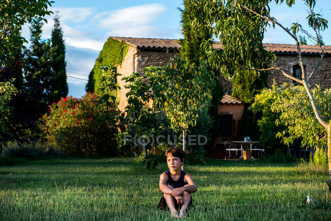 Boy sitting in garden of farmhouse — Stock Photo