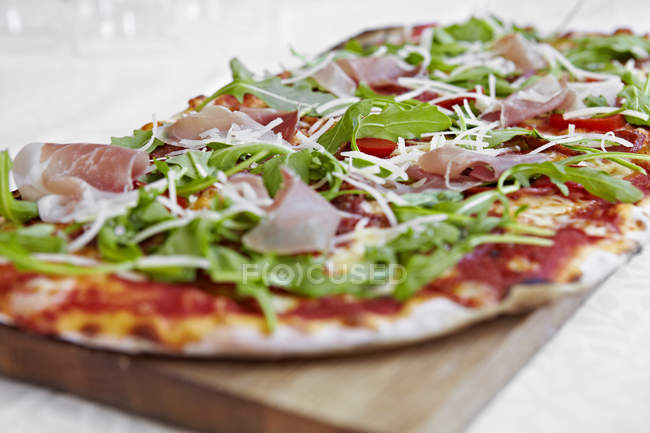 Fresh pizza with rocket and parma ham on chopping board — Stock Photo