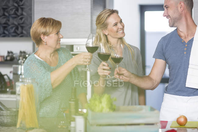 Tre amici in cucina con bicchieri di vino — Foto stock