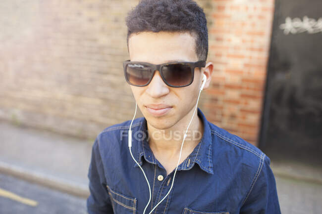 Портрет молодого чоловіка на відкритому повітрі, в сонцезахисних окулярах та навушниках — стокове фото