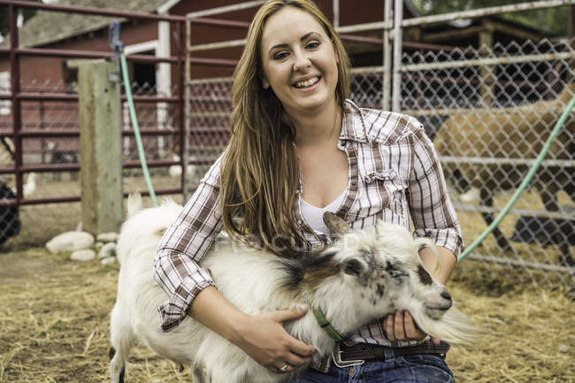 Portrait of young woman petting goat on ranch, Bridger, Montana, USA — Stock Photo
