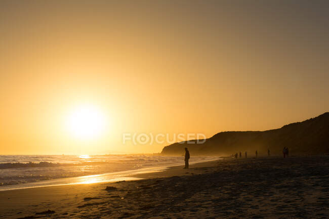 Turistas retroiluminados en la playa dorada del atardecer, Newport Beach, California, EE.UU. - foto de stock
