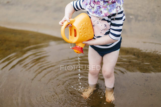 Menina pé tornozelo profundo no lago derramando água da lata de rega de brinquedos, Huntsville, Canadá — Fotografia de Stock