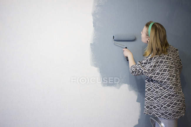 Junge Frau auf Leiter klebt graue Farbe an Hauswand — Stockfoto