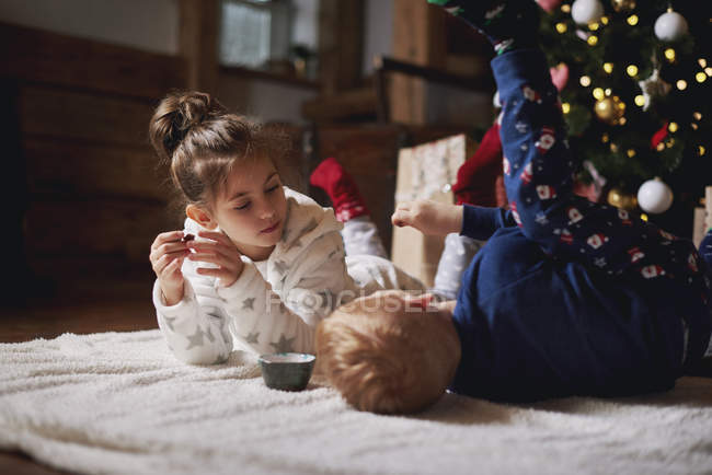 Young girl and boy relaxing beside Christmas tree — Stock Photo