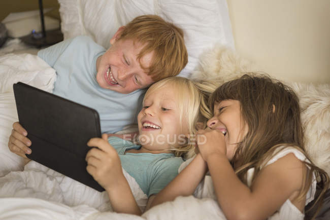 Дети лежат в постели и смотрят на цифровой планшет — стоковое фото
