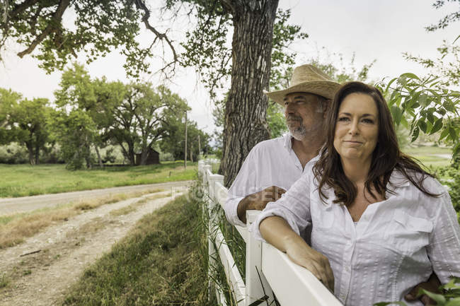 Parejas maduras apoyadas contra la cerca del rancho, Bridger, Montana, Estados Unidos - foto de stock