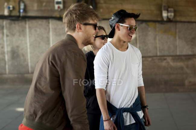 Três amigos caminhando debaixo da ponte, sorrindo — Fotografia de Stock