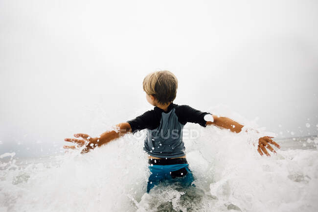 Niño caminando en olas, vista trasera - foto de stock