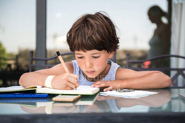 Junge am Tisch schreibt in Arbeitsbuch — Stockfoto