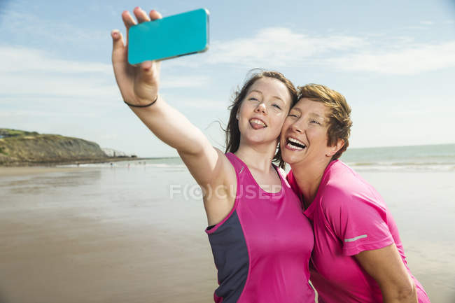 Madre e hija tomando selfie en la playa - foto de stock