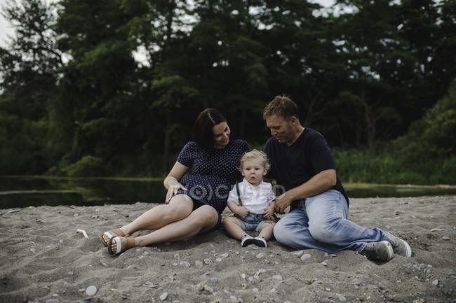Pregnant couple sitting on beach with male toddler son, Lake Ontario, Canada — Stock Photo