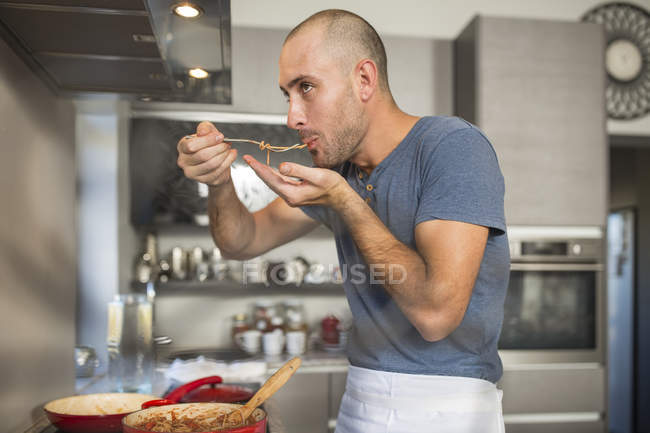 Hombre en la cocina degustación de alimentos de tenedor - foto de stock