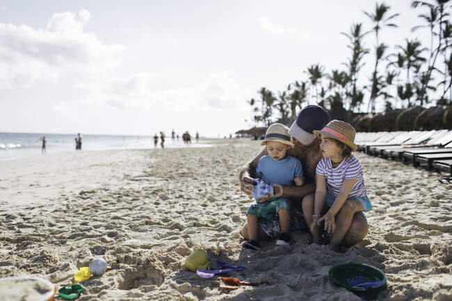 Батько сидить з молодим сином і дочкою на пляжі — стокове фото