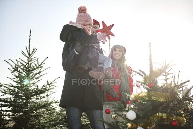 Girl and parents placing star on forest christmas tree — Stock Photo