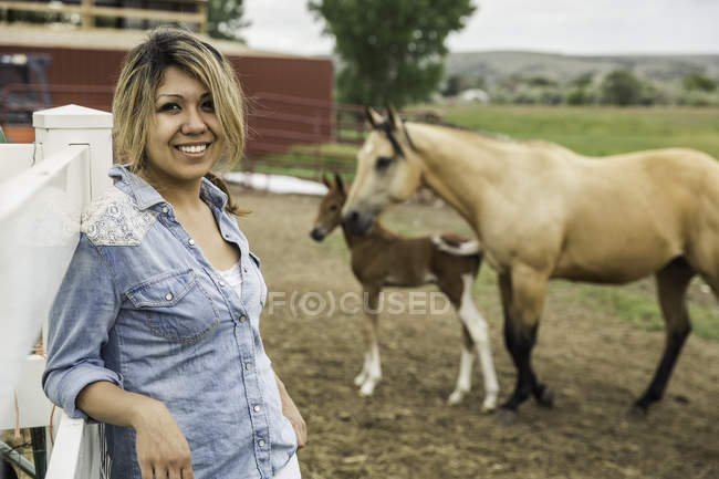 Портрет молодой женщины на ферме, лошади и жеребенка на заднем плане — стоковое фото