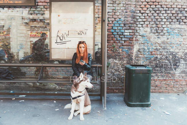 Рыжая женщина с собакой ждет на автобусной остановке — стоковое фото