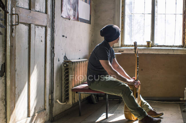 Junger Mann sitzt auf Stuhl und hält Gitarre — Stockfoto