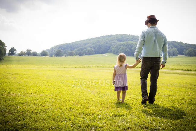 Rear view of girl strolling with father in rural field — Stock Photo