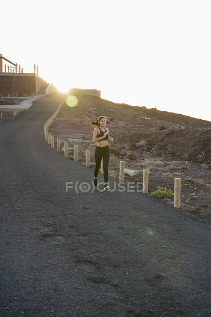 Jovem fêmea correndo na estrada rural ao pôr do sol, Las Palmas, Ilhas Canárias, Espanha — Fotografia de Stock