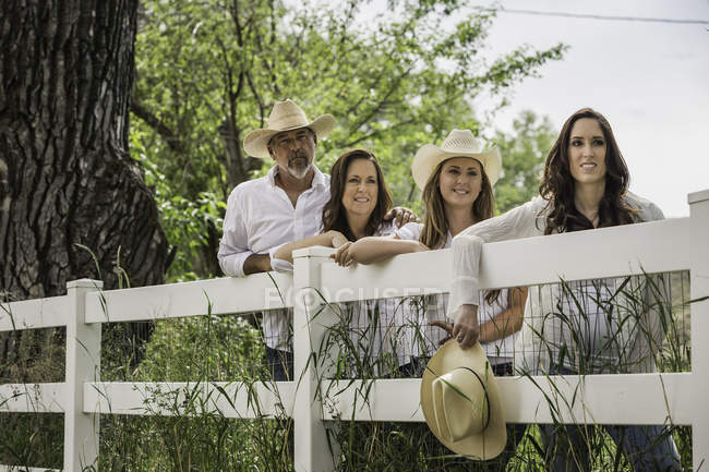 Retrato de pareja adulta y dos hijas en sombreros de vaquero apoyados contra la cerca del rancho, Bridger, Montana, EE.UU. - foto de stock