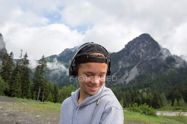 Portrait of teenage boy wearing headphones against mountains — Stock Photo