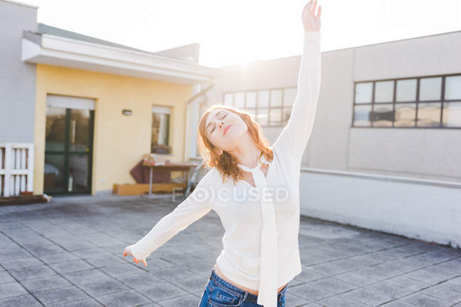 Jeune femme dansant sur une terrasse ensoleillée avec les yeux fermés — Photo de stock