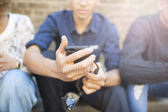 Три друзі сидять на вулиці, дивлячись на смартфон — стокове фото