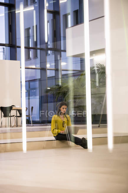 Jeune femme utilisant un ordinateur portable sur le sol du bureau — Photo de stock