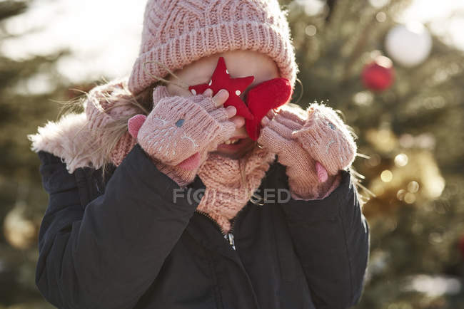 Menina na floresta de árvore de natal cobrindo seus olhos com decorações de Natal — Fotografia de Stock