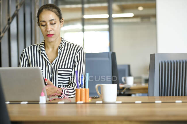 Empresaria sentada en el escritorio, usando laptop - foto de stock