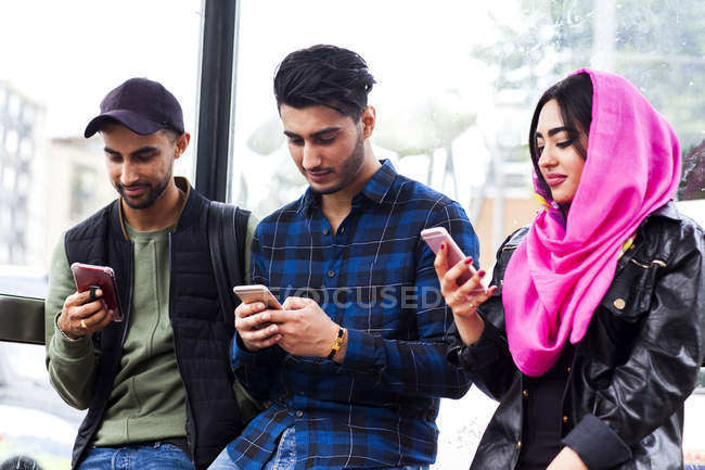Three friends in row looking at smartphones — Stock Photo