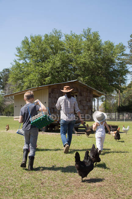 Mother and two children working on farm, walking towards chicken coop, rear view — Stock Photo