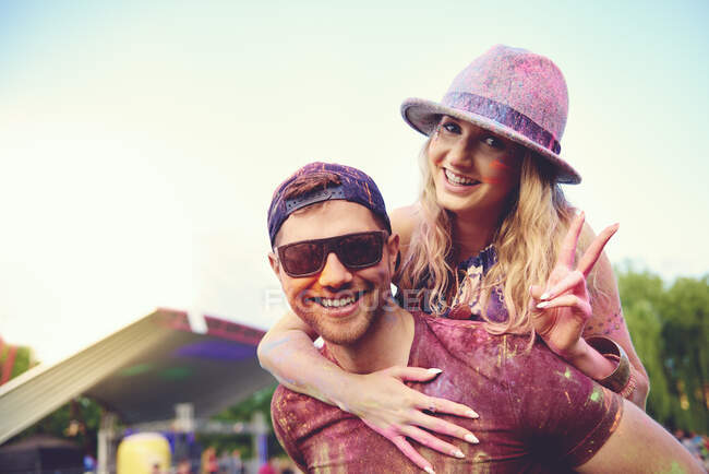 Portrait of young woman covered in coloured chalk powder getting boyfriend piggyback at festival — Stock Photo