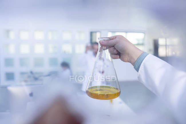 Trabajador de laboratorio sosteniendo vaso de precipitados de vidrio, que contiene líquido amarillo - foto de stock