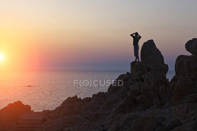 Silhouette d'homme sur des rochers regardant le coucher du soleil sur la mer, Olbia, Sardaigne, Italie — Photo de stock