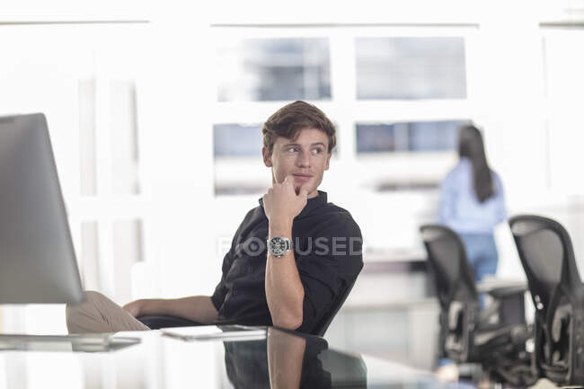 Young male office worker looking over his shoulder from office desk — Stock Photo