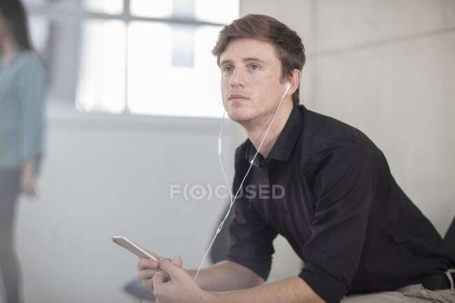 Young male office worker daydreaming at desk listening to earphones — Stock Photo