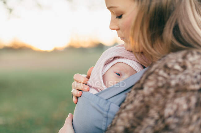 Mãe e bebê filha ao ar livre, mãe carregando o bebê no sling bebê, vista lateral — Fotografia de Stock
