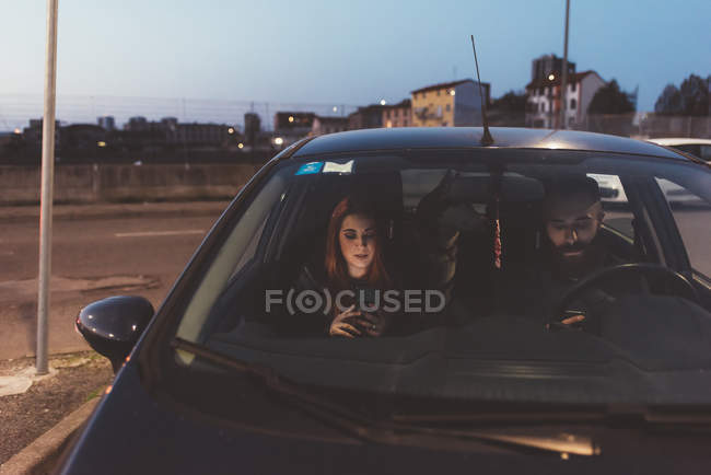 Casal no carro à noite usando smartphones — Fotografia de Stock