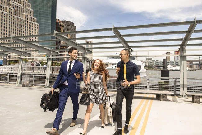Businessmen and woman with luggage walking and talking on waterfront — Stock Photo