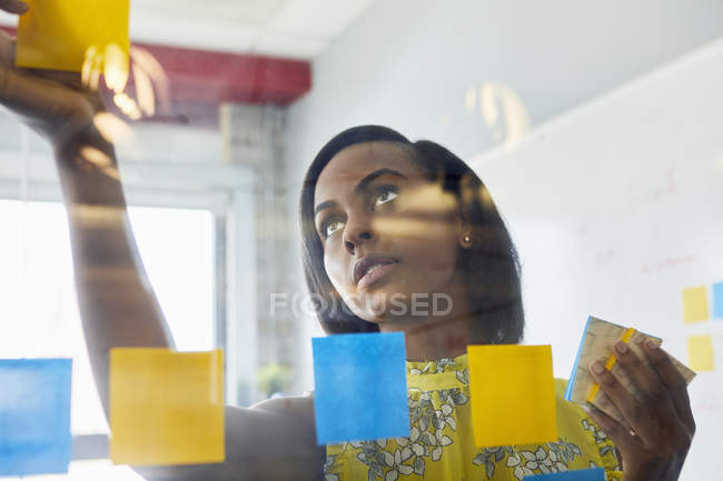 Молодая женщина в офисе прилипает записки к стеклу в офисе — стоковое фото