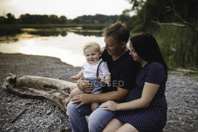 Pregnant couple sitting on beach log with male toddler son, Lake Ontario, Canada — Stock Photo