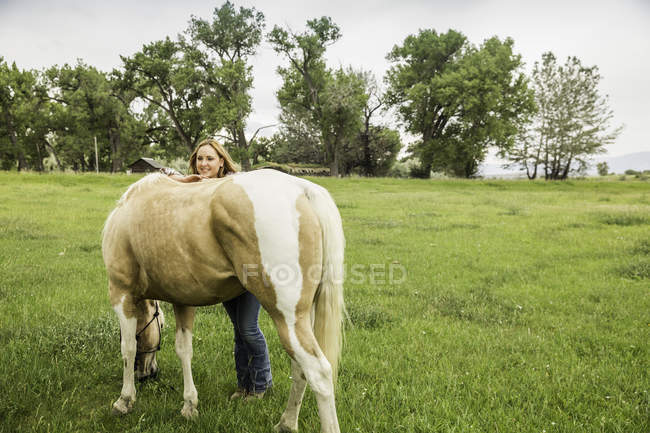 Mujer joven con caballo de pastoreo en el campo de rancho, Bridger, Montana, EE.UU. - foto de stock