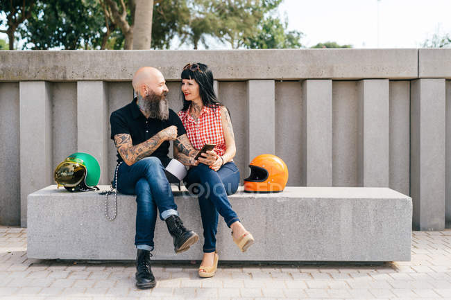 Tatuado maduro hipster pareja sentado en concreto banco - foto de stock