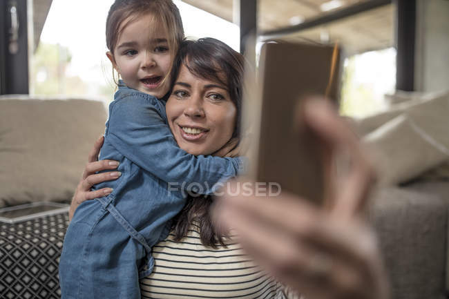 Madura mujer tomando selfie con hija en sala de estar - foto de stock