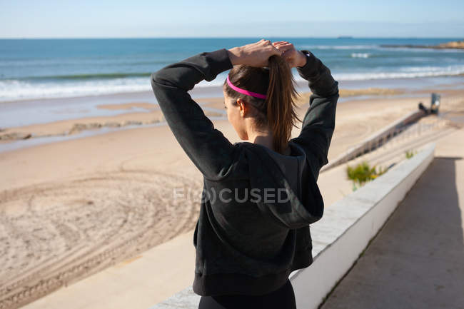 Vista trasera de la joven en la playa atando el pelo en cola de caballo, Carcavelos, Lisboa, Portugal, Europa - foto de stock