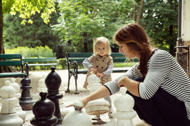 Madre e hija pequeña jugando con ajedrez gigante en el parque - foto de stock