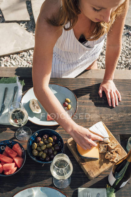 Jovem mulher ao ar livre cortando queijo do quadro de queijo — Fotografia de Stock